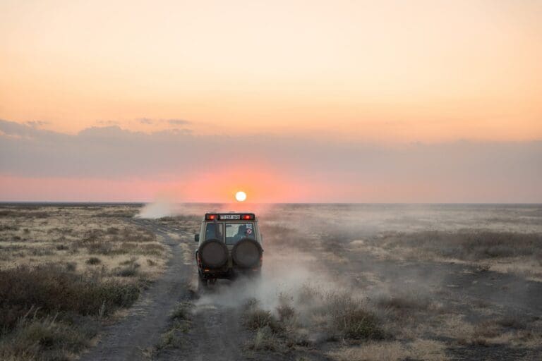 safari jeep driving through dusty plains at sunset