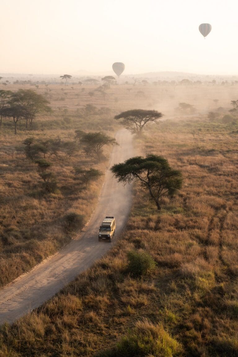safari jeep driving on dusty road with hot air balloons
