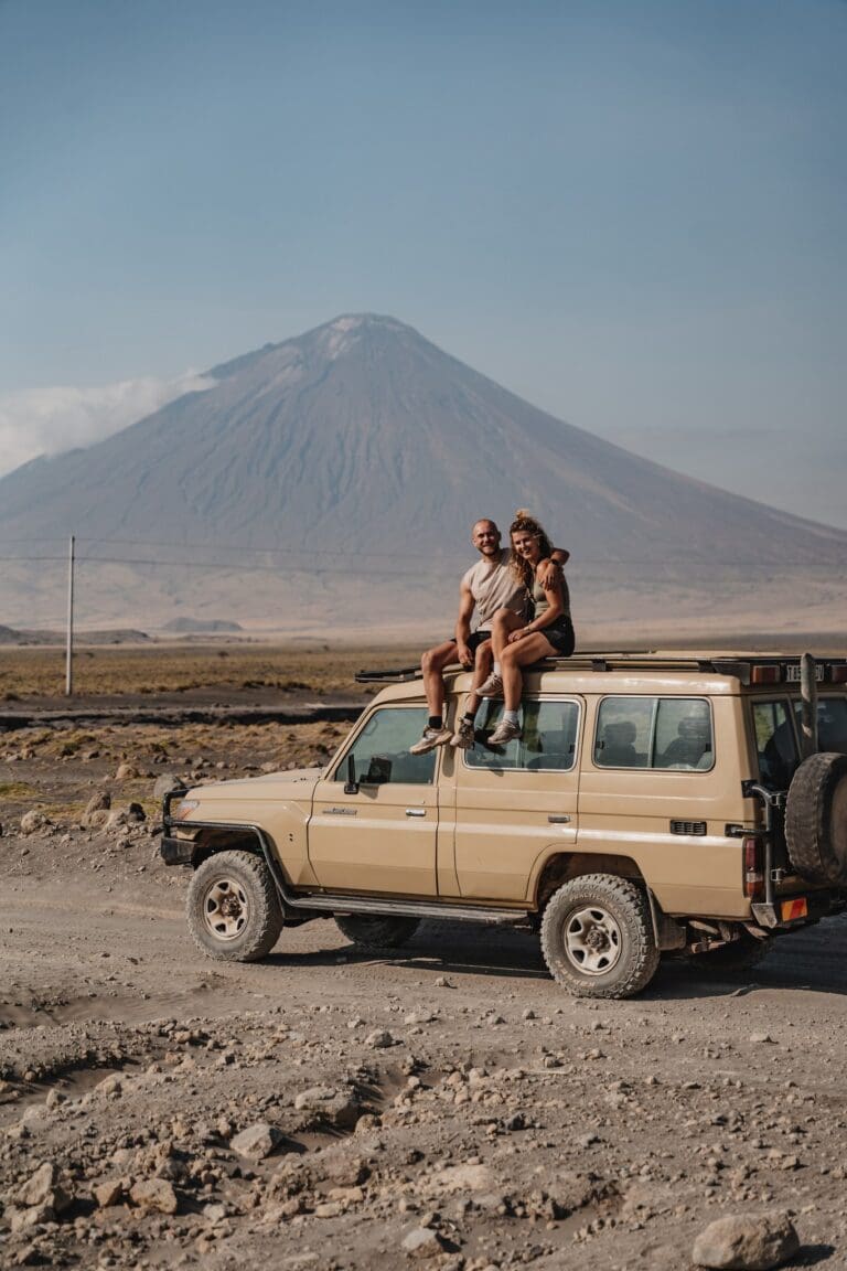 couple on safari jeep roof with volcano in background